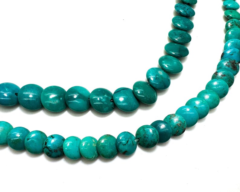 May include: A strand of round, flat turquoise beads arranged in two curved rows. The beads feature a vibrant teal-blue color with natural dark brown matrix veining throughout, creating a smooth, polished surface texture on each individual bead.