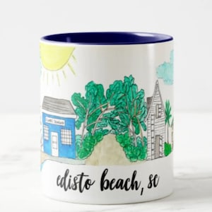 May include: White ceramic coffee mug with a blue rim. The mug features a hand-drawn illustration of a beach scene with houses, trees, and a sun. The text "Edisto Beach, SC" is written in black at the bottom of the mug.
