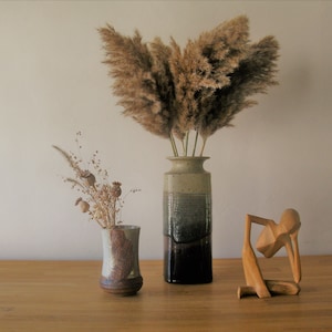 Puede incluir: Dos jarrones de cerámica con hierba de la pampa seca y vainas de semillas de amapola secas, y una escultura de madera de una persona sentada con la cabeza en las manos.