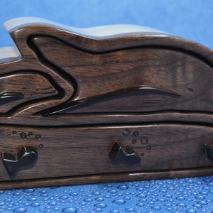May include: A wooden box shaped like a dolphin with three drawers. The box is dark brown with black accents and has a carved dolphin design.