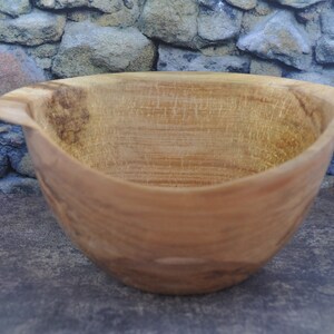 May include: A large, wooden bowl with a natural, light brown finish. The bowl has a wide, rounded base and a slightly flared rim. It is made from a single piece of wood and has a smooth, polished surface.