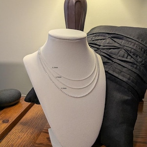 May include: Three silver-toned beaded chains displayed on a beige mannequin bust. The chains are labeled with their respective widths of 1.2mm, 1.5mm, and 2.2mm, showing the varying thickness of the small, round, metallic beads linked together.
