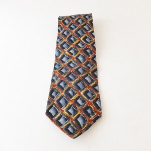 May include: A patterned necktie with a repeating geometric design. The tie features a pattern of blue, yellow, and red diamonds on a dark background. The tie is made of a smooth fabric and is suitable for formal or business attire.