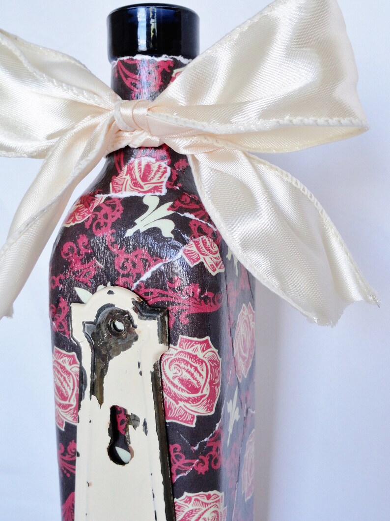 May include: A glass bottle with a black and white floral design and a white satin bow. The bottle has a vintage keyhole design on the front.