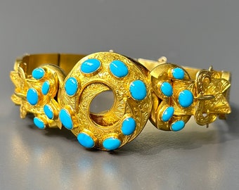 Puede incluir: Un brazalete de oro con un diseño circular adornado con piedras turquesa. El brazalete está intrincadamente detallado con motivos florales y tiene un cierre de bisagra.
