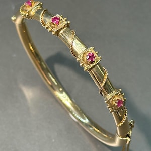 Puede incluir: Un brazalete de oro con un diseño de cuerda trenzada y cuatro piedras de rubí rojo engastadas en biseles cuadrados.