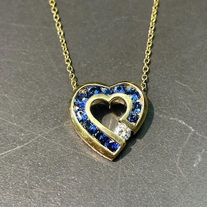 May include: A gold chain necklace with a heart-shaped pendant. The pendant is set with blue sapphires and a single diamond.