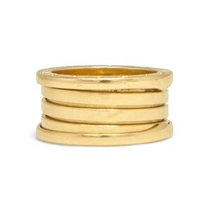 May include: A gold ring featuring a multi-band design with a smooth, polished finish. The ring consists of several stacked, interconnected horizontal bands that create a cylindrical shape with a flat top and bottom edge, showcasing a metallic lustre.