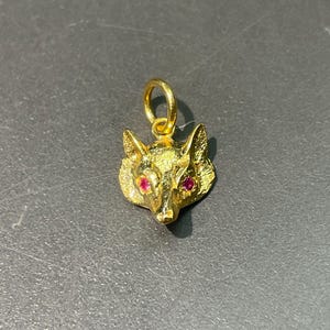 Puede incluir: Un dije de cabeza de zorro de oro con ojos de rubí rojo. El dije tiene un bucle en la parte superior para sujetarlo a un collar o pulsera.