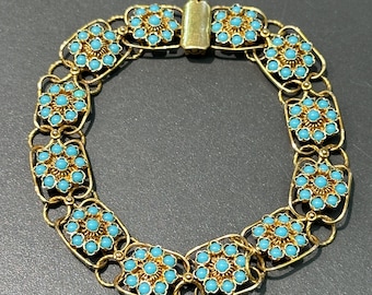 Puede incluir: Un brazalete de oro con un diseño de cadena de eslabones. Cada eslabón está decorado con un grupo de piedras de color azul turquesa.