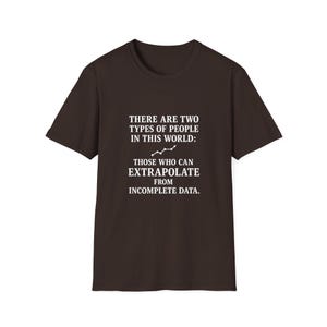 May include: A dark brown t-shirt with white text that reads: "THERE ARE TWO TYPES OF PEOPLE IN THIS WORLD: THOSE WHO CAN EXTRAPOLATE FROM INCOMPLETE DATA." The shirt has a crew neck and short sleeves.