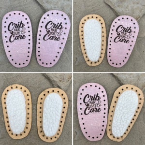 May include: Oval-shaped baby shoe soles with pre-punched holes along the edges. Some soles are light pink with a glitter finish and the black text 'Crib hair dont care' with a pacifier icon, while others feature a white sherpa-textured lining.