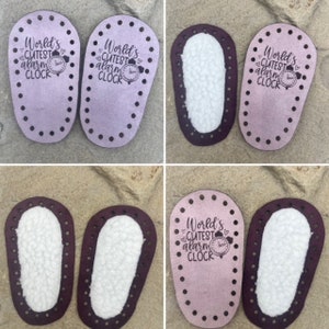 Puede incluir: Dos suelas de zapato ovaladas de material morado claro con agujeros preperforados en los bordes. Las suelas presentan el texto impreso en negro World's CUTEST alarm CLOCK con un icono de reloj y corazones. Algunas tienen forro de lana blanca.