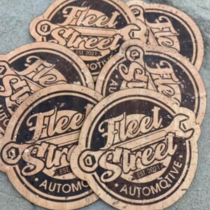 Peut inclure: Une collection de dessous de verre circulaires en liège avec un logo imprimé marron foncé. Le motif comprend le texte Fleet Street, l'année EST. 2021 et le mot AUTOMOTIVE, accompagnés d'une illustration graphique d'une clé au centre.