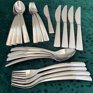 May include: A set of stainless steel flatware including four spoons, three forks, and five knives arranged in a group. The utensils feature a polished, reflective finish with smooth, tapered handles and a simple, clean design for dining use.