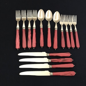 Könnte beinhalten: Set aus Besteck mit roten Griffen und goldenen Akzenten. Das Set enthält Gabeln, Löffel und Messer.