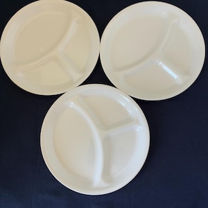 May include: Three cream-coloured, divided plates. Each plate features three sections, ideal for portion control. The plates are round and made of a smooth material. The plates are arranged on a dark blue surface.