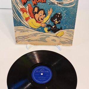 May include: Vintage vinyl record featuring "Mighty Mouse Saves Dinky" by Paul Terry. The album cover shows Mighty Mouse in a yellow outfit and red cape, with a black duck. The record is black with a blue RCA Victor label.