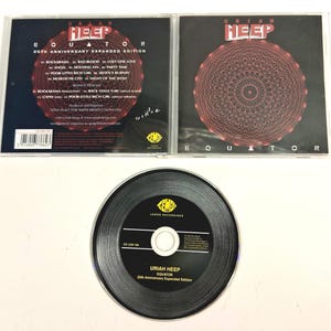 May include: A CD set of the album "Equator" by Uriah Heep, featuring a black CD and two jewel cases. The cases display the album title and tracklist, with a red and black design. The CD has the album title and the Lemon Recordings logo.