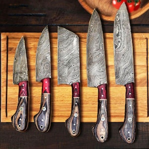 Puede incluir: Cinco cuchillos de cocina con mangos de madera y hojas de acero Damasco. Los cuchillos están dispuestos en una tabla de cortar de madera.
