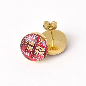 May include: A pair of gold stud earrings featuring a red circuit board design. The earrings are made of metal and have a post back.