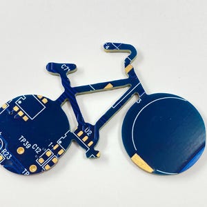 Puede incluir: Un circuito impreso en forma de bicicleta azul y dorado con el texto "TPS9 C12" y "R23" impreso en &eacute;l.