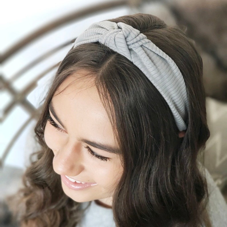 May include: A gray knotted headband made of a soft, ribbed fabric. The headband is worn on a person's head.