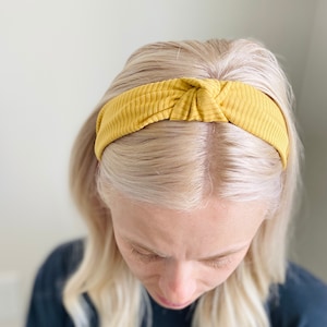 May include: A yellow knotted headband made of a ribbed fabric.