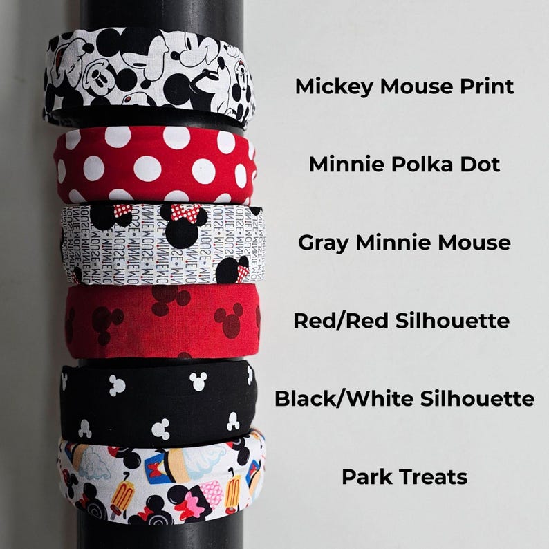 May include: Six fabric headbands stacked vertically on a dark cylinder. Patterns include: Mickey Mouse Print, Minnie Polka Dot, Gray Minnie Mouse, Red/Red Silhouette, Black/White Silhouette, and Park Treats, with corresponding text labels to the right.