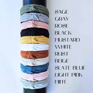 May include: A stack of 11 knotted headbands in various colors, including sage, gray, rose, black, mustard, white, rust, beige, slate blue, light pink, and mint.