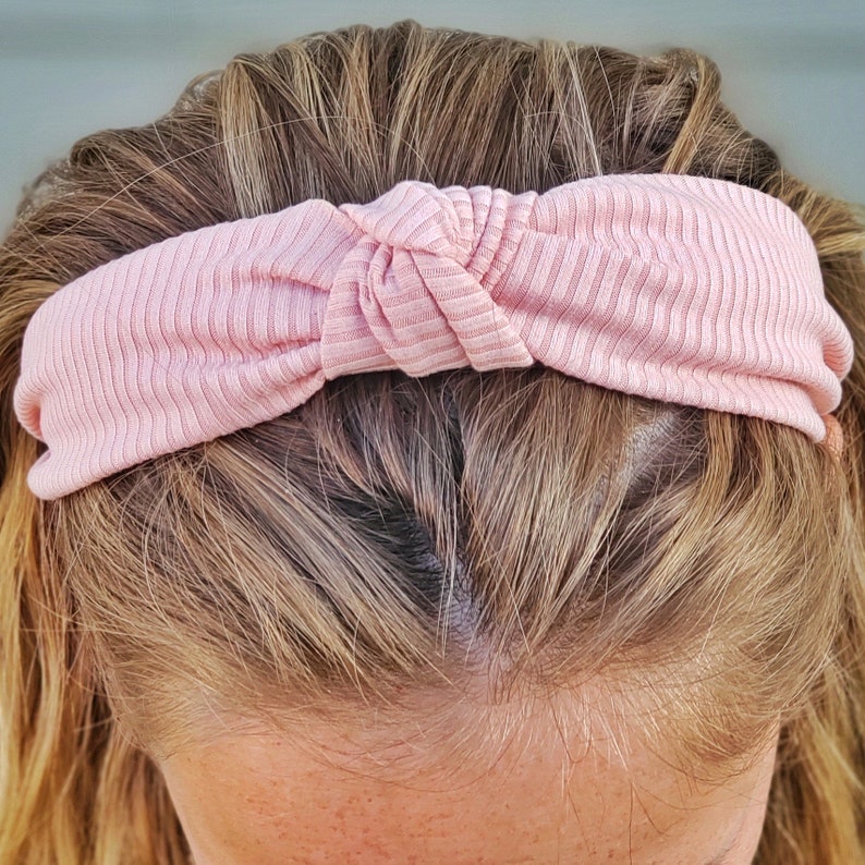 May include: A pink knotted headband made of a soft, ribbed fabric. The headband is worn on a person's head.