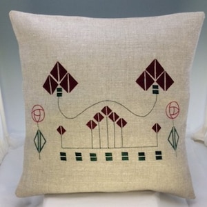 May include: A beige linen pillow with an embroidered design in shades of burgundy, green, and white. The design features stylized flowers and geometric shapes.