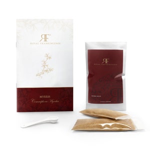 May include: A white package with the text "Royal Frankincense" and a gold logo. The package contains a small bag of brown powder labeled "Myrrh Resin".