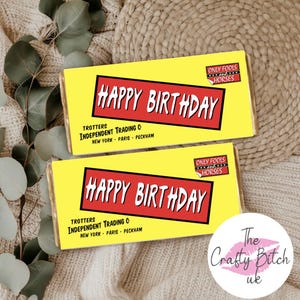 Könnte beinhalten: Zwei gelbe Schokoriegelverpackungen mit den Worten "HAPPY BIRTHDAY" in einem roten Rechteck. Die Verpackungen enthalten auch den Text "Trotters Independent Trading Co" und "Only Fools and Horses". Der Hintergrund ist ein beiges Strickgewebe.