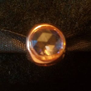 Puede incluir: Un charm de oro rosa con una piedra preciosa púrpura transparente en el centro.