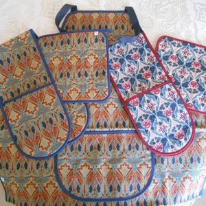 May include: A set of four kitchen pot holders and an apron with a blue, red and gold floral pattern. The pot holders have a navy blue trim and the apron has navy blue trim and straps.