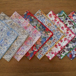 May include: A set of eight square fabric handkerchiefs arranged in a row, each featuring a distinct floral pattern with intricate botanical illustrations. The edges of each handkerchief are finished with a thin, solid-colored stitched border.