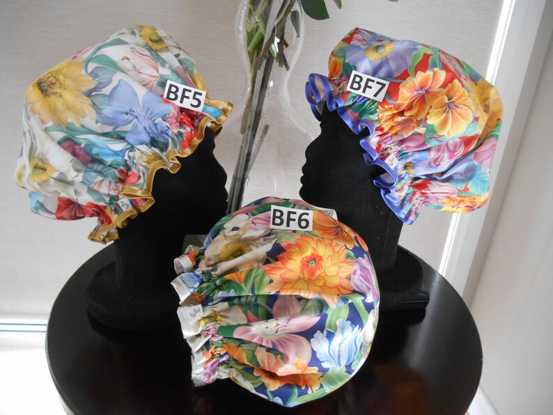 K&ouml;nnte beinhalten: Drei Duschhauben mit Blumenmustern. Die Hauben sind mit BF5, BF6 und BF7 beschriftet. Die Hauben werden auf schwarzen Schaufensterpuppen ausgestellt.