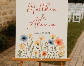 Pode incluir: Um cartaz de casamento branco com uma borda floral e o texto "Welcome to the Wedding of Matthew & Alexa August 17, 2024" em letras vermelhas. O cartaz está em um cavalete de madeira.