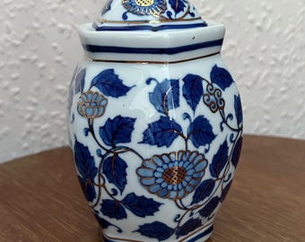 Peut inclure: Un pot en porcelaine blanche avec un motif floral bleu et or. Le pot a un couvercle et est hexagonal.