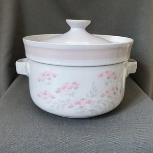 Puede incluir: Plato de cerámica blanco para hornear con un diseño floral rosa y una tapa. El plato tiene dos asas a los lados.