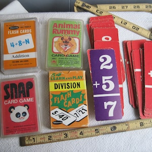 May include: A collection of vintage educational card games, including Animal Rummy, Snap, Addition Flash Cards, and Division Flash Cards. The cards feature colorful illustrations and simple math problems.