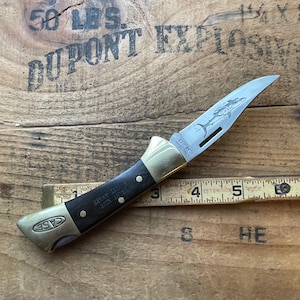 Puede incluir: Una navaja plegable Case XX con una hoja de acero inoxidable con un dise&ntilde;o de delf&iacute;n grabado. El mango es negro con refuerzos y remaches de lat&oacute;n. La navaja mide aproximadamente 10 cm de largo cuando est&aacute; cerrada. La hoja tiene el texto "CASE XX" y "SAFETY AWARD".