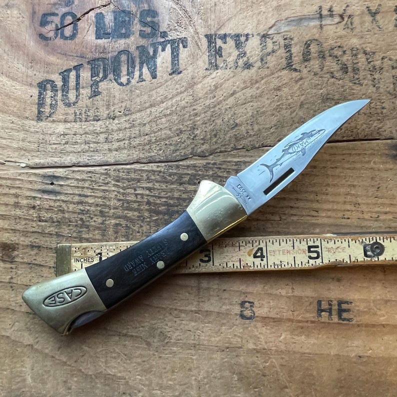 Puede incluir: Una navaja plegable Case XX con una hoja de acero inoxidable con un dise&ntilde;o de delf&iacute;n grabado. El mango es negro con refuerzos y remaches de lat&oacute;n. La navaja mide aproximadamente 10 cm de largo cuando est&aacute; cerrada. La hoja tiene el texto "CASE XX" y "SAFETY AWARD".