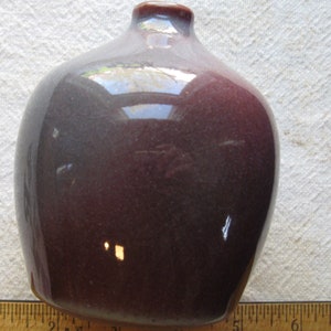 May include: A glossy, rounded vase with a dark burgundy and gray gradient. The vase has a narrow neck and a smooth, reflective surface. The ceramic vessel is a decorative item.