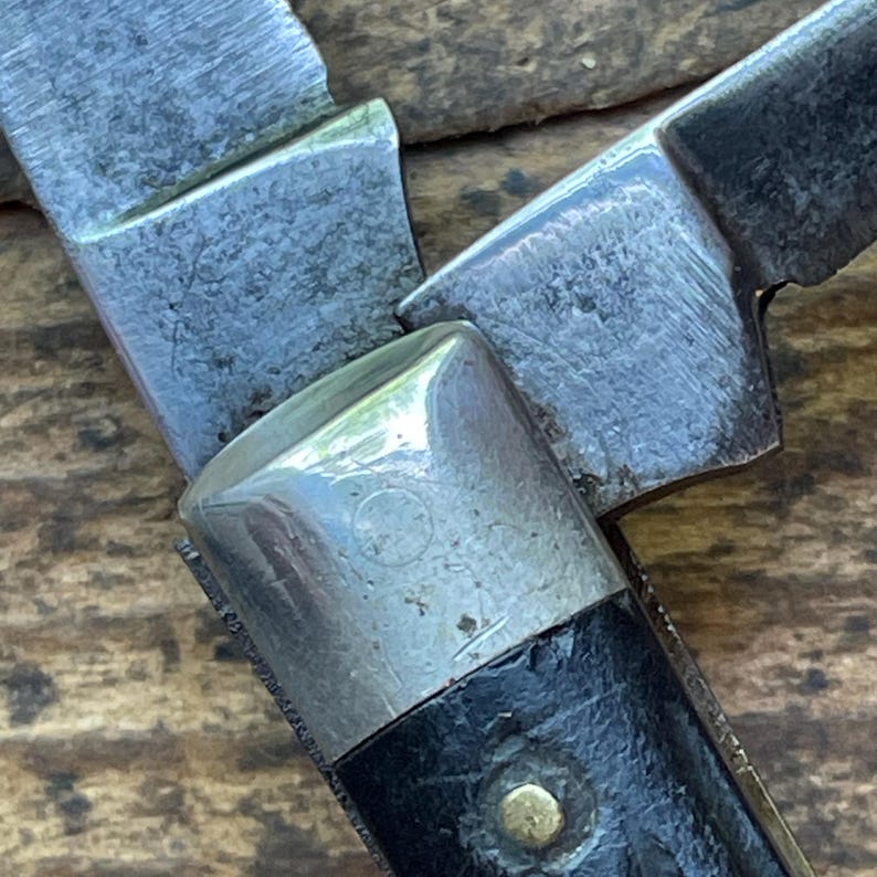 May include: Close-up of a vintage pocket knife with a partially open blade. The knife features a silver bolster, a black handle, and a brass rivet. The blades show signs of wear, indicating age and use. The knife is a classic tool.