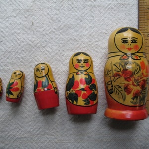 May include: A set of six traditional Russian nesting dolls, or Matryoshka dolls, in varying sizes. The dolls are painted with a yellow base, red skirts, and floral designs. The largest doll is approximately 6 inches tall.