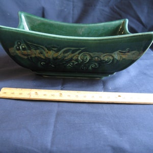 May include: A green ceramic planter with a square base and a decorative gold design. The planter has a wide, shallow shape and is perfect for displaying plants or flowers.