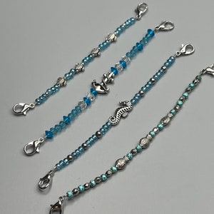 May include: Four beaded bracelets with silver-tone lobster clasps. The bracelets feature blue and clear beads, with silver charms of sea creatures, including fish, seahorses, and anchors. The beads are strung on a clear cord.