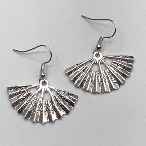 May include: A pair of silver-colored fan-shaped earrings. Each earring features a detailed, openwork design with a decorative pattern. The earrings have a hook closure for pierced ears and are displayed against a white background.